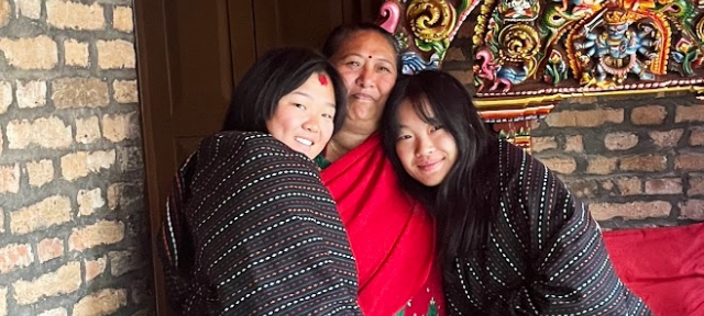 Three people smiling with arms around each other in front of a colorful sculpture.