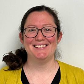 Jaimie is smiling at the camera. She has a yellow top, glasses, and her dark hair is pulled back into a ponytail. 