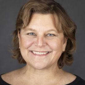 Jessica is smiling at the camera. The background is gray and she has cropped hair and a black top.