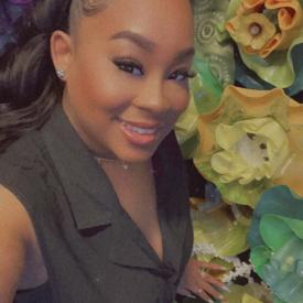 A woman in a gray vest smiling in front of glass flowers