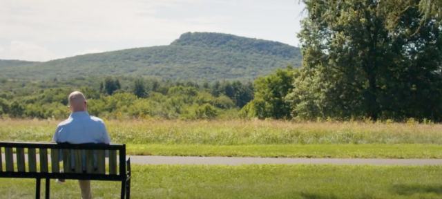 Dean of Faculty Gary Hawkins sits on a bench staring out at mountains.