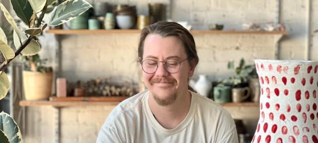 Lucas Mays in his studio with red dotted pottery