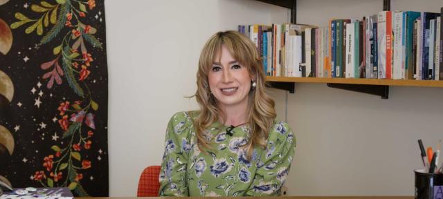 Jina Fast is sitting in her office wearing a green dress.