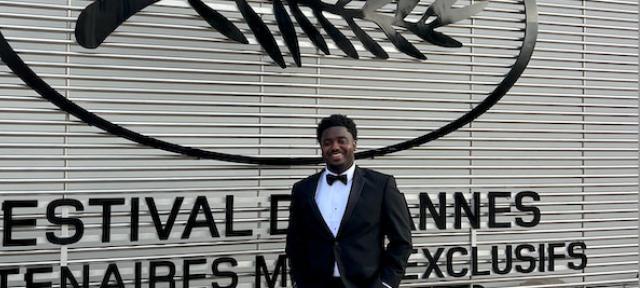 Jacory Martin, in a tuxedo, smiling in front of a sign at Cannes