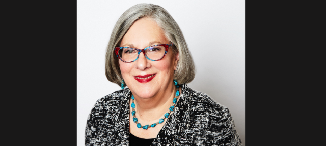 A person in glasses smiling against a white background.
