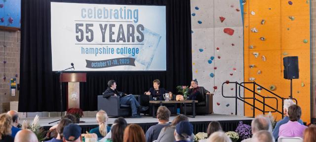 Ken Burns, Lynn Pasquerella, and Gary Marcus sit on a stage under a banner reading Celebrating 55 Years