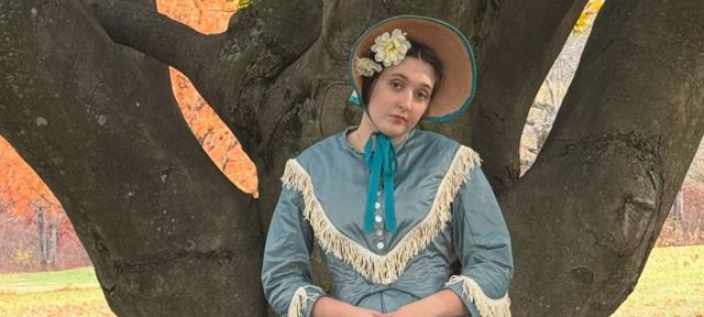 Lila Maher staning in period dress next to a tree