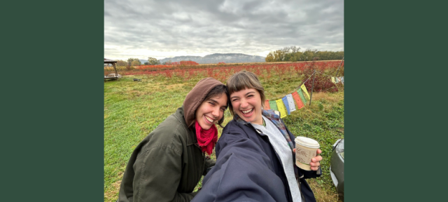 Two people taking a selfie and smiling with a green landscape in the background.