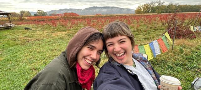 Two people taking a selfie and smiling with a green landscape in the background.