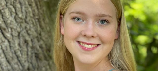 A person in a tank top stands by a tree smiling.