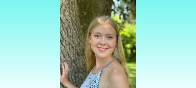 A person in a tank top stands by a tree smiling.