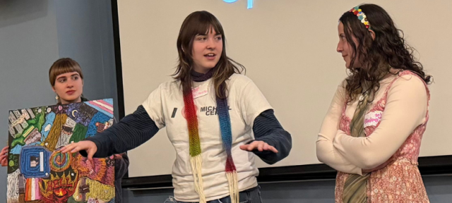 Three people standing in front of a whiteboard talking; one is holding a board game.