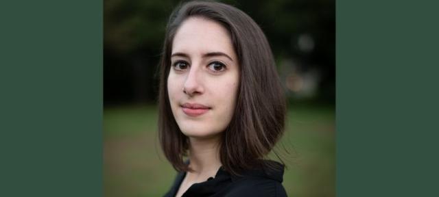 A close up of a person with a brown bob and a black shirt standing outside.