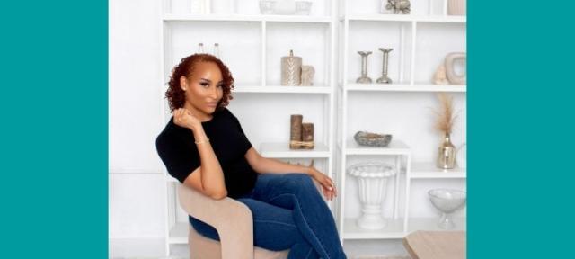 A person sits on a chair sideways in front of a shelf with books and decorative items.