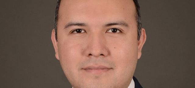 A headshot of Manny Castro in front of a plain brown background