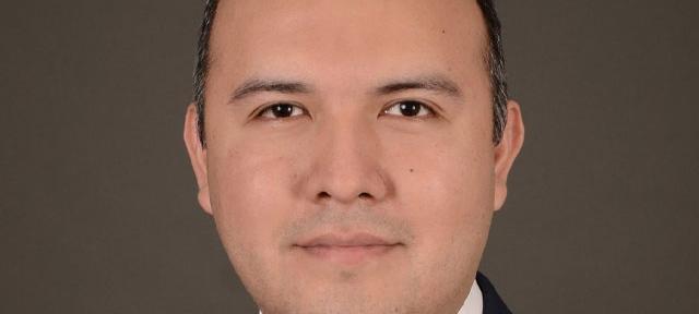 A headshot of Manny Castro in front of a plain brown background