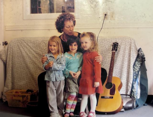 A woman sits on a couch with three children in her lap and a guitar to the side.