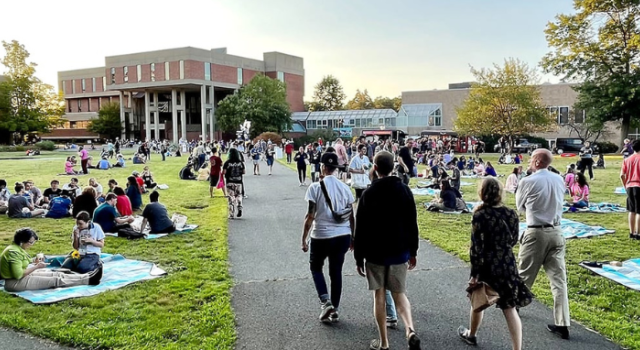 A sunset photo of Hampshire College's library lawn filled with new students and their friends and family. 