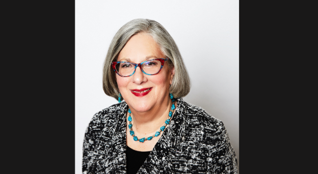 A person in glasses smiling against a white background.