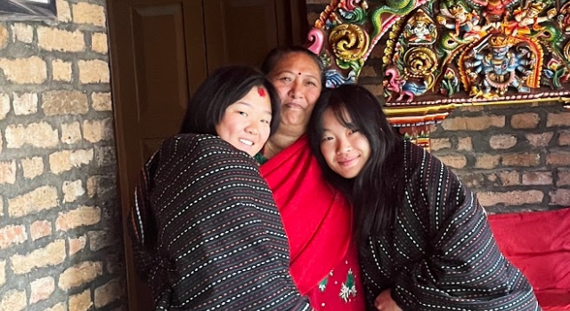 Three people smiling with arms around each other in front of a colorful sculpture.