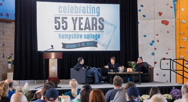 Ken Burns, Lynn Pasquerella, and Gary Marcus sit on a stage under a banner reading Celebrating 55 Years