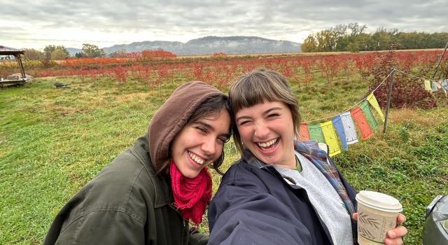 Two people taking a selfie and smiling with a green landscape in the background.