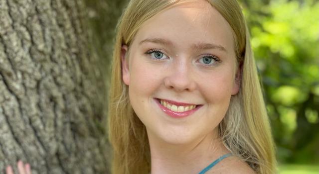 A person in a tank top stands by a tree smiling.