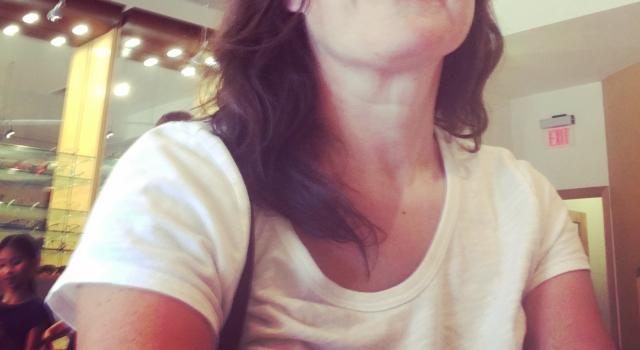 A person in glasses and a white t-shirt looking up.