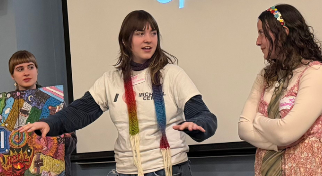 Three people standing in front of a whiteboard talking; one is holding a board game.