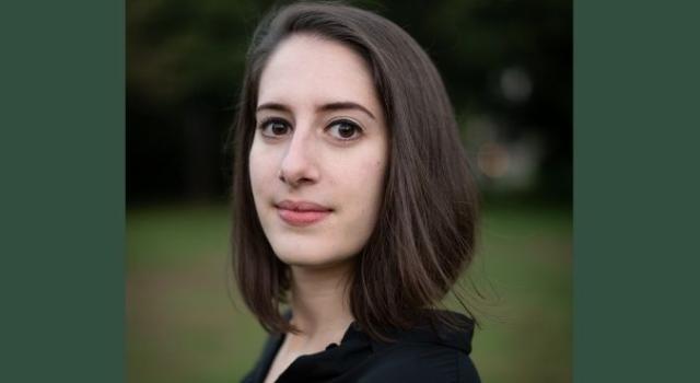 A close up of a person with a brown bob and a black shirt standing outside.