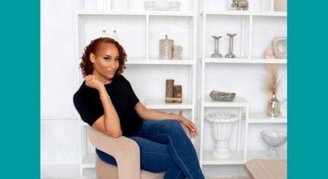 A person sits on a chair sideways in front of a shelf with books and decorative items.