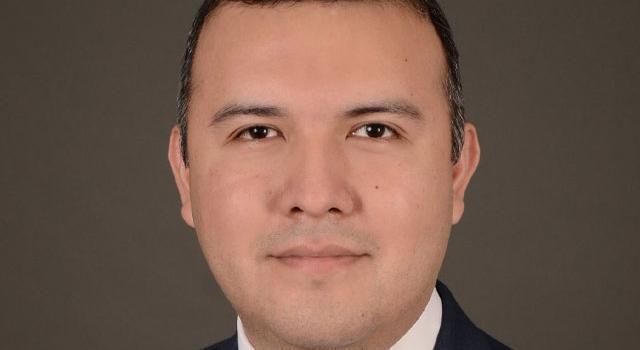 A headshot of Manny Castro in front of a plain brown background