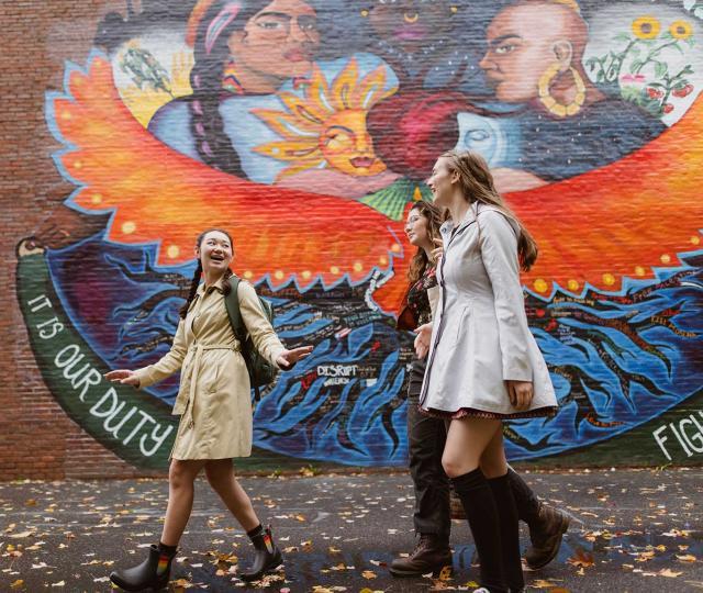 Three students walk past a mural. 