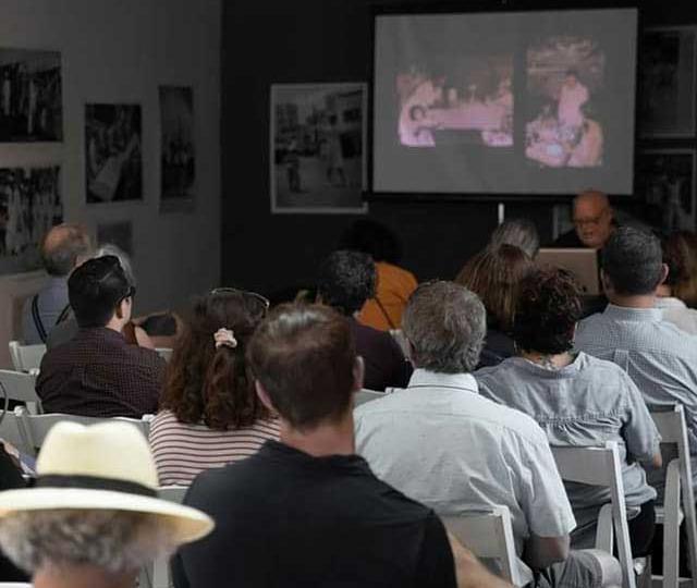 Opening weekend artist's talk by Pablo Delano for the exhibition The Museum of the Old Colony, 2018. A group of seated visitors face a projector screen presentation and the Artist.
