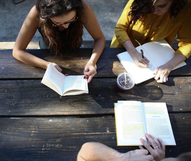 Three people writing on a picnic table.