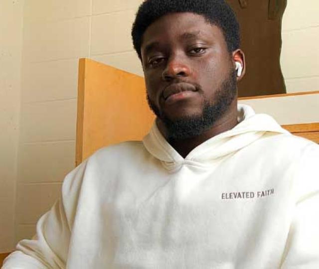 Rupert Tawiah-Quashie F22 wears a white sweatshirt and looks into the camera. He is sitting at a desk.