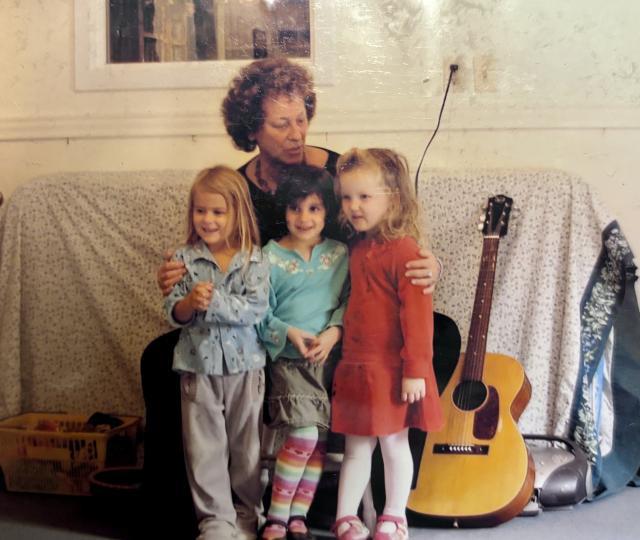 A woman sits on a couch with three children in her lap and a guitar to the side.