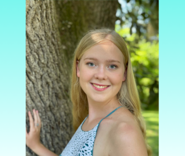 A person in a tank top stands by a tree smiling.