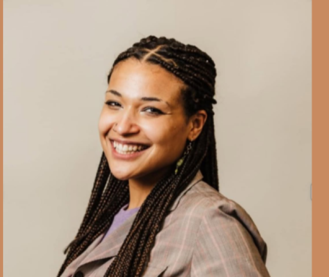 A woman turning toward the camera and smiling wearing a taupe shirt in front of a beige background.