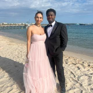 Two people in formal wear standing on a shoreline.