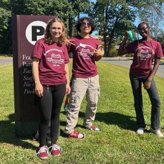 Students in burgundy t-shirts stanging and smiling at camera