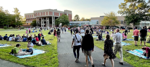 A sunset photo of Hampshire College's library lawn filled with new students and their friends and family. 