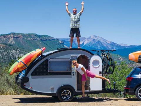 Earl stands atop camper with arms up and Glenna stands in door with leg out
