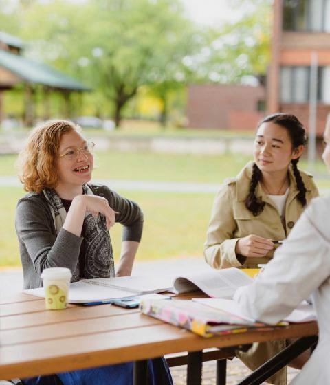 Students sitting outside talking at a picnic table.