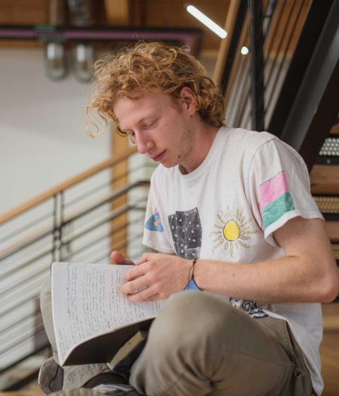 Student sitting on stairs writing in notebook.
