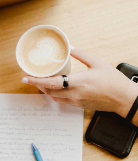 Hand holding a coffee over a notebook.