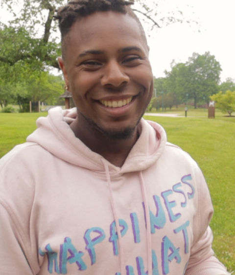 Aaron Andrew smiles at the camera. There is a jar of body butter shown on the right side.