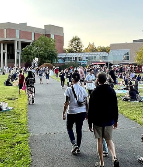 A sunset photo of Hampshire College's library lawn filled with new students and their friends and family. 