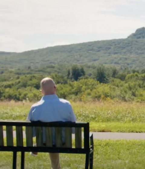 Dean of Faculty Gary Hawkins sits on a bench staring out at mountains.