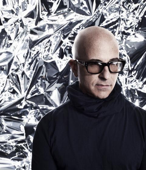 A person in glasses and a black turtleneck standing in front of a silver backdrop.